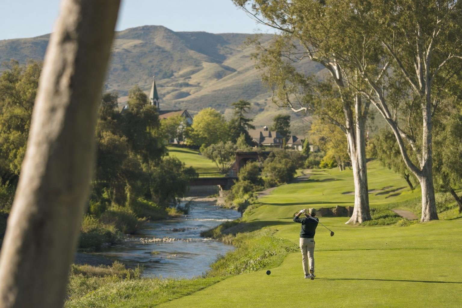 A golf course along a river lined with sycamore trees in a ranch valley near a Danish-style town (AI-generated image)