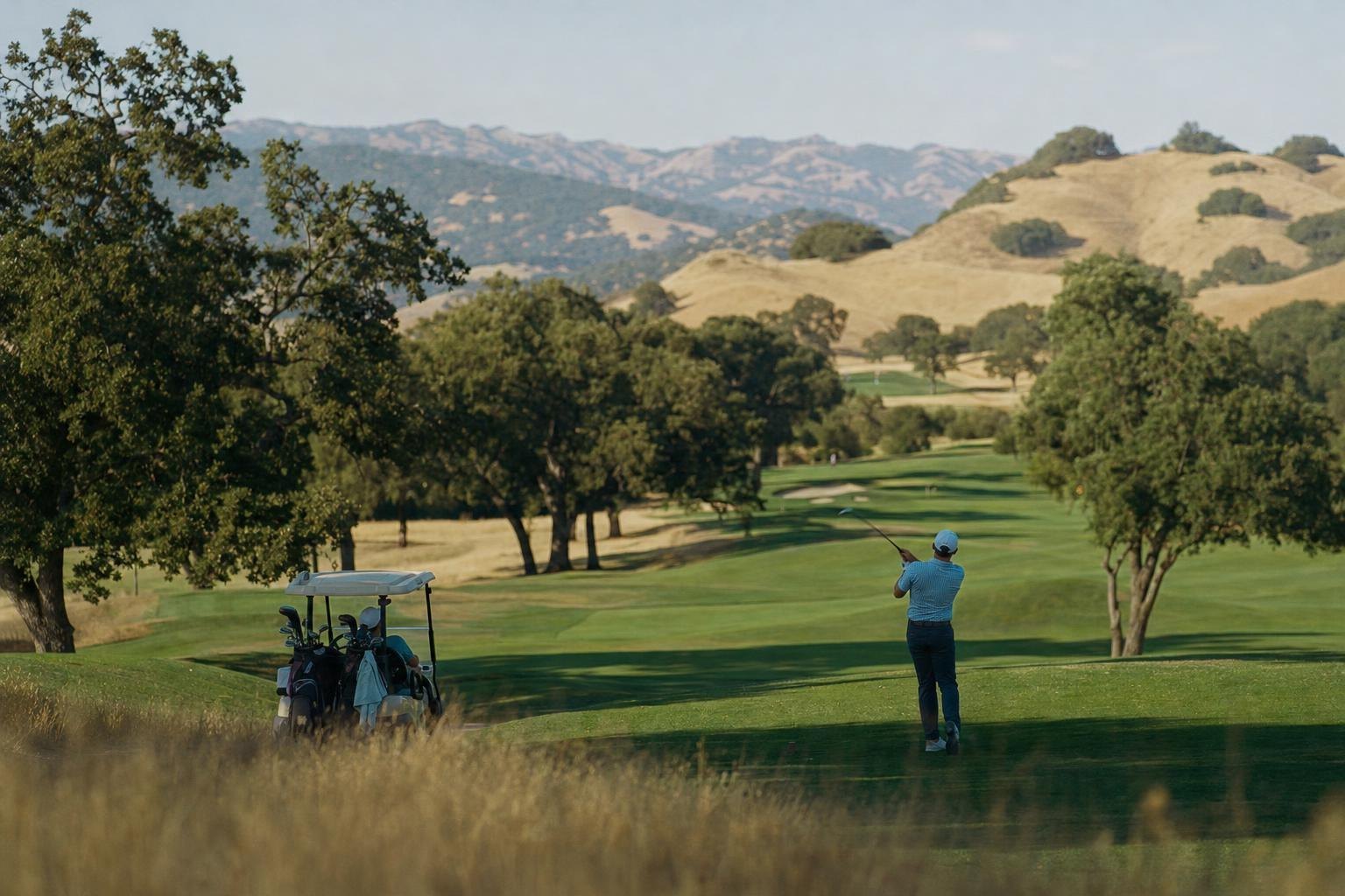 Wide view of an oak-lined parkland golf course in a California valley, green fairways against golden hills (AI-generated image)