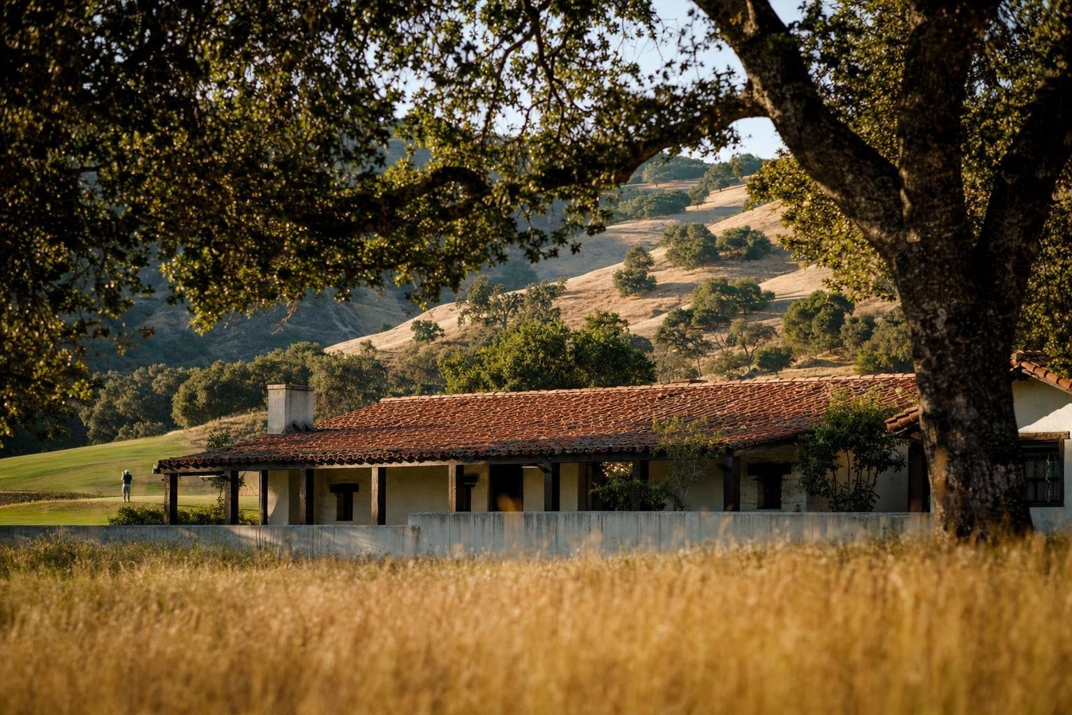 An old adobe ranch building with a tiled roof under great oak trees, golden hills, timeless (AI-generated image)