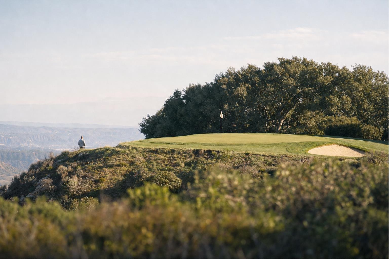 A short par-three green on a high mesa with a cream flag, oak trees behind, wide sky (AI-generated image)