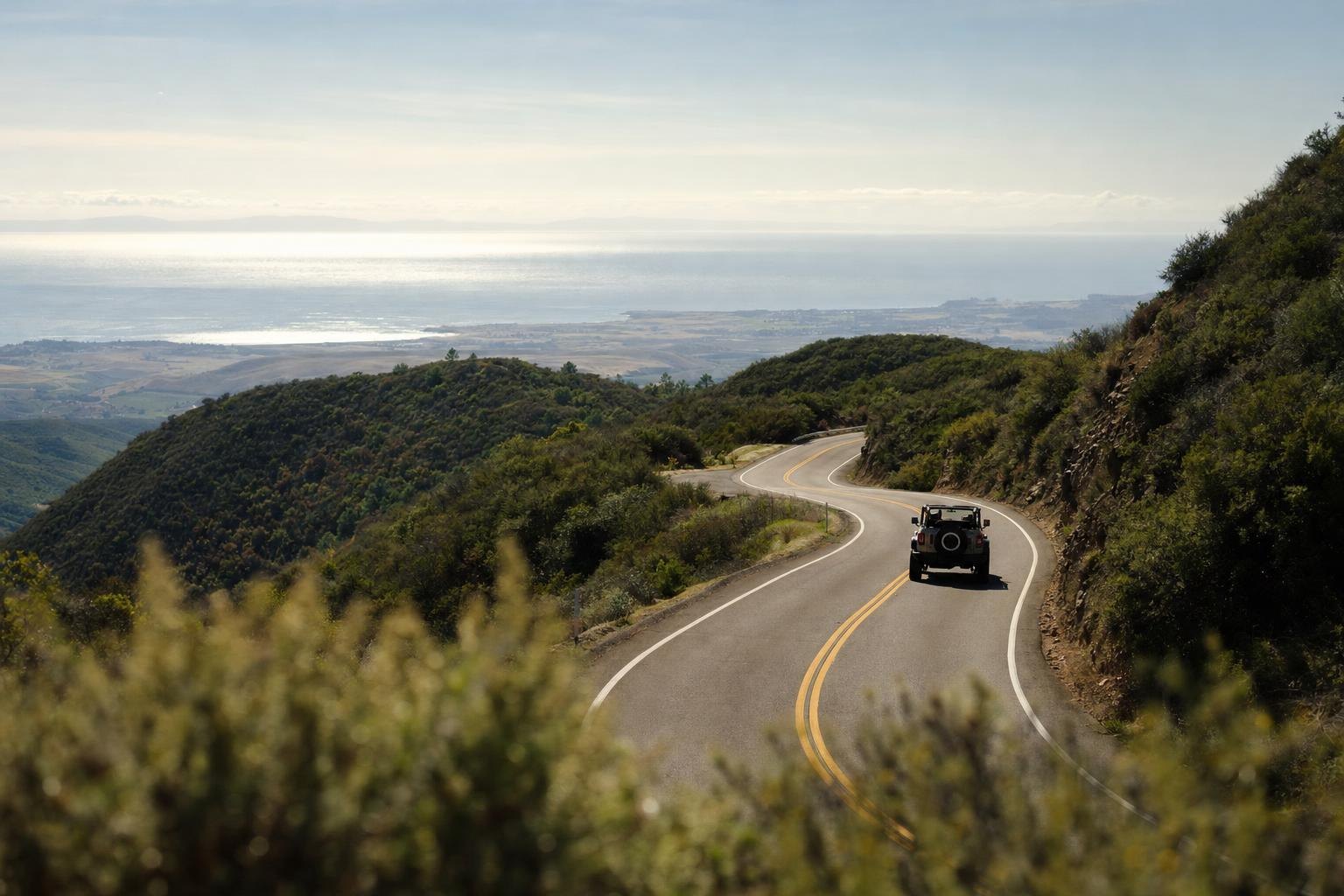A two-lane mountain highway winding over a pass with chaparral and views to the ocean, Santa Ynez mountains (AI-generated image)