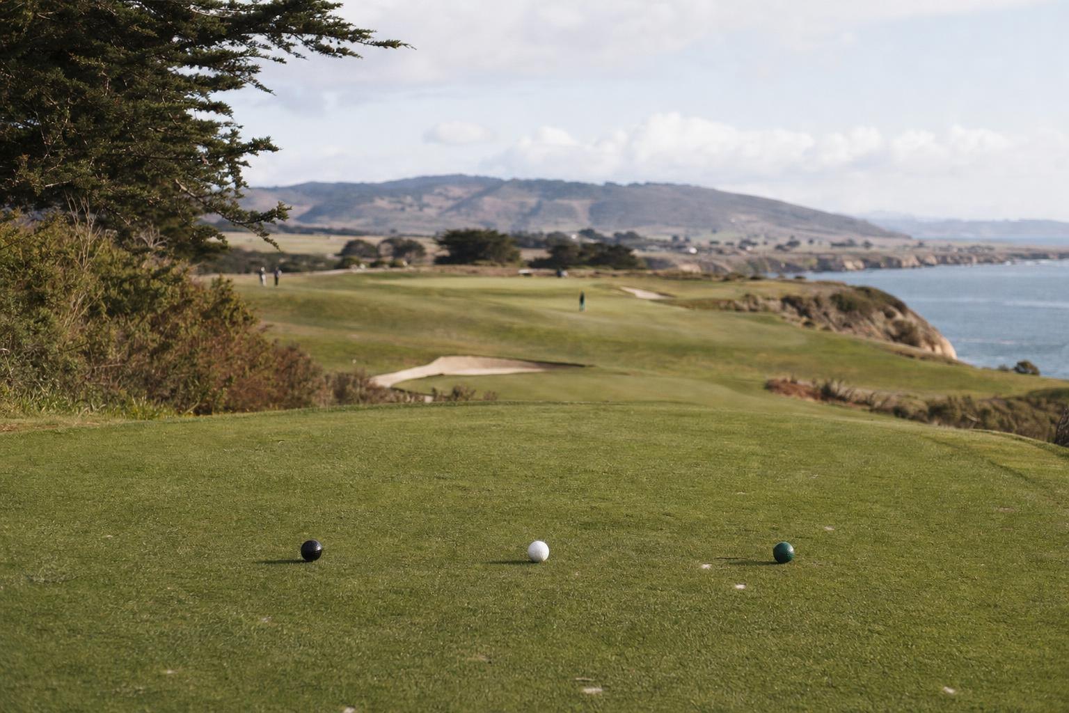 Three tee markers (black, white and green) on a tee box with a fairway beyond (AI-generated image)